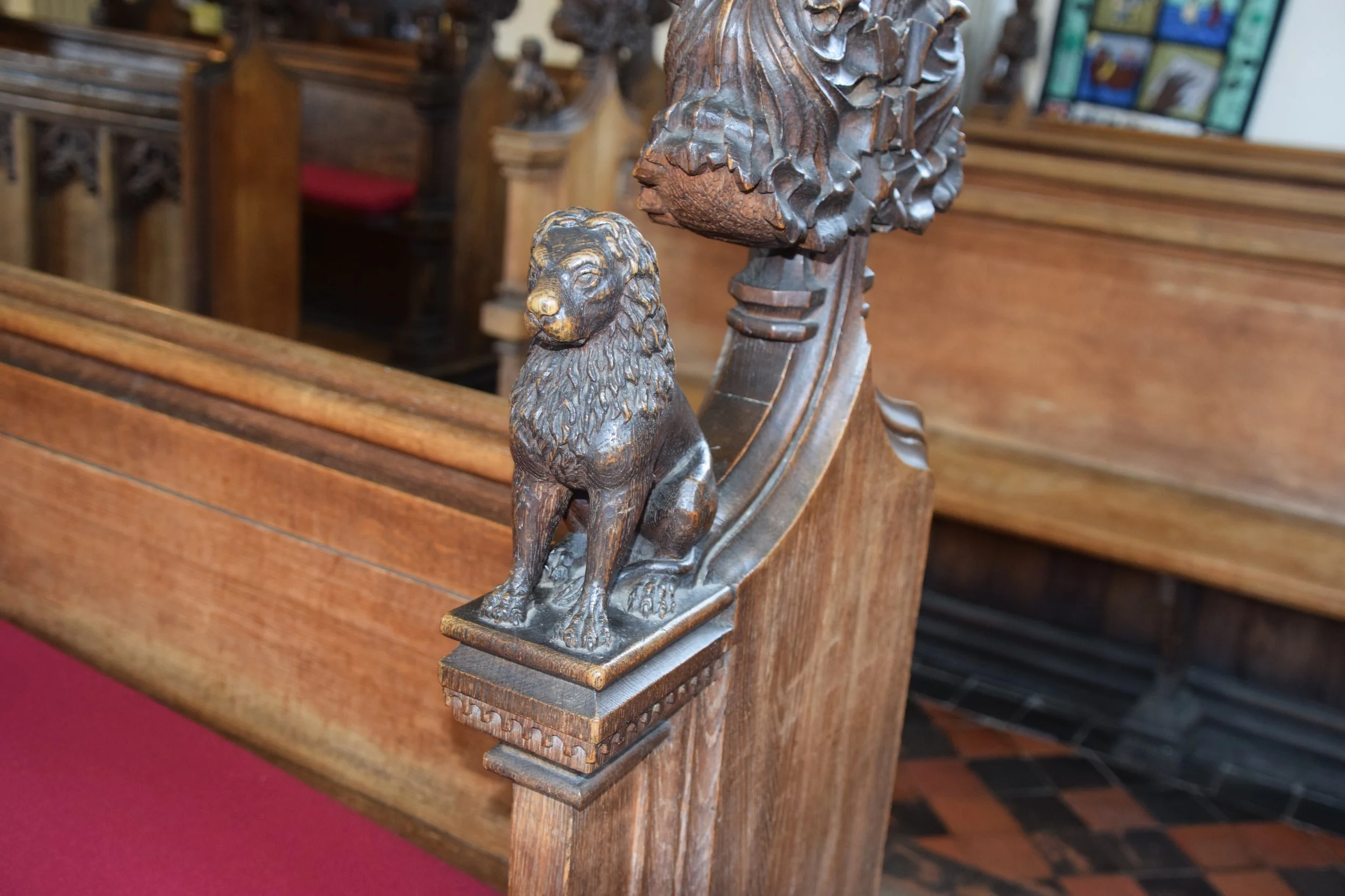 Carved wooden lion finial on an ornate church pew beside dark wood paneling and stained glass