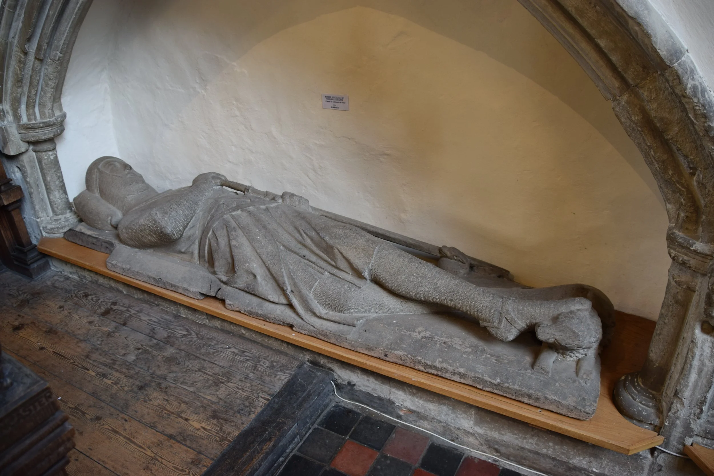 Medieval stone effigy of a reclining armored knight displayed inside a historic church beneath a stone arch