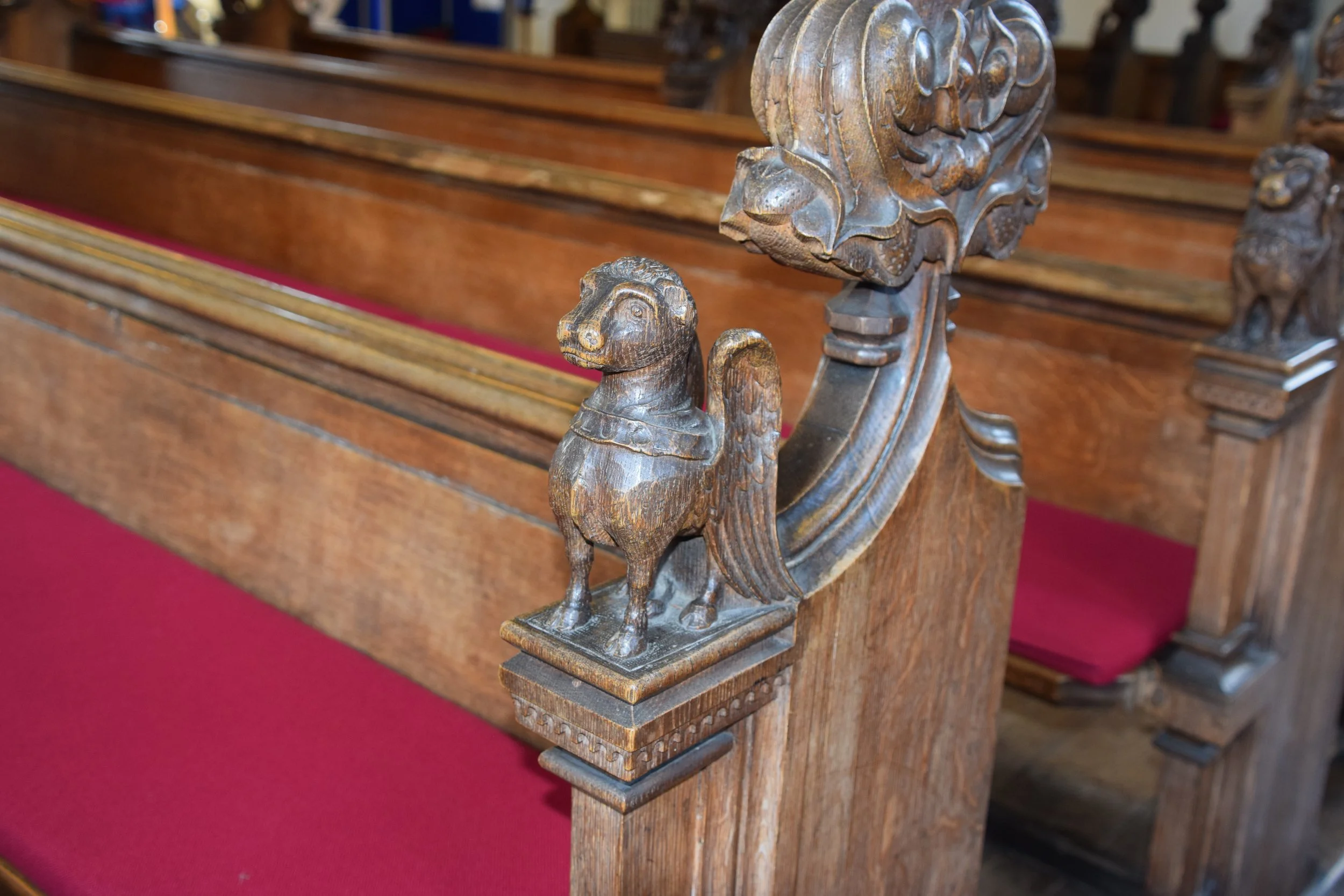 Ornate carved wooden church pew end featuring a small dog statue and a large winged mythical creature