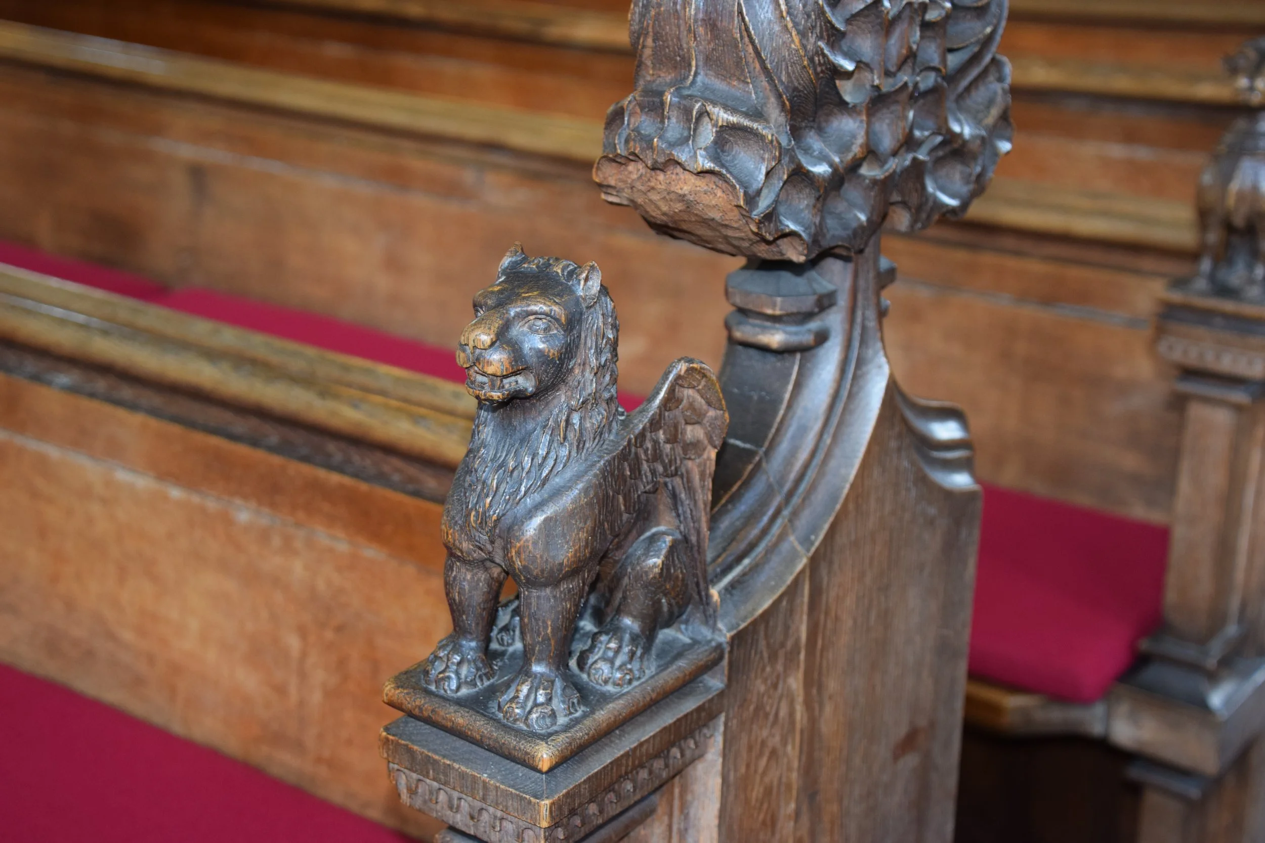 Carved wooden lion ornament on an ornate church pew with red carpet