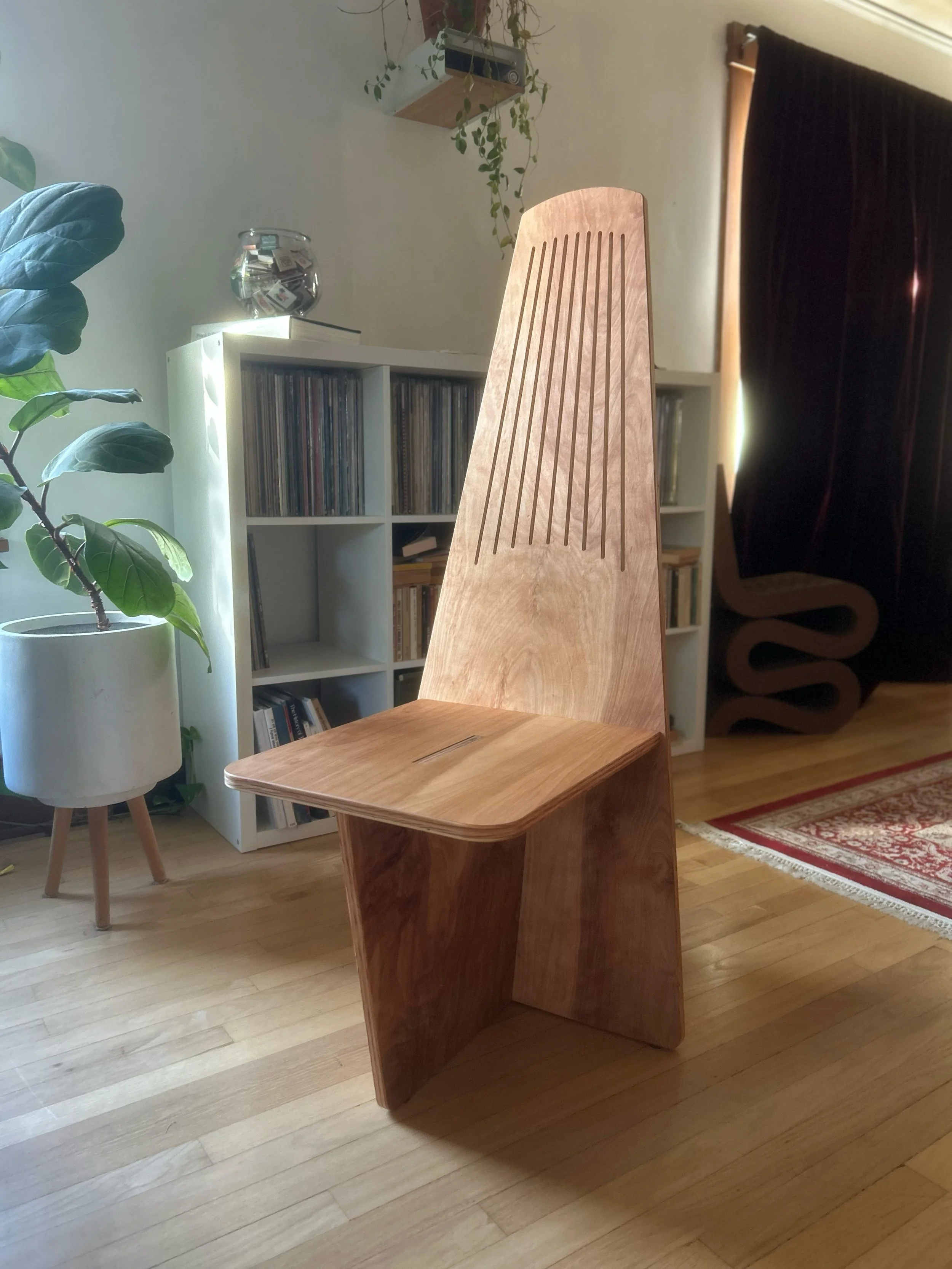 Modern wooden chair in a sunlit living room with potted plants, record shelves, and a patterned rug