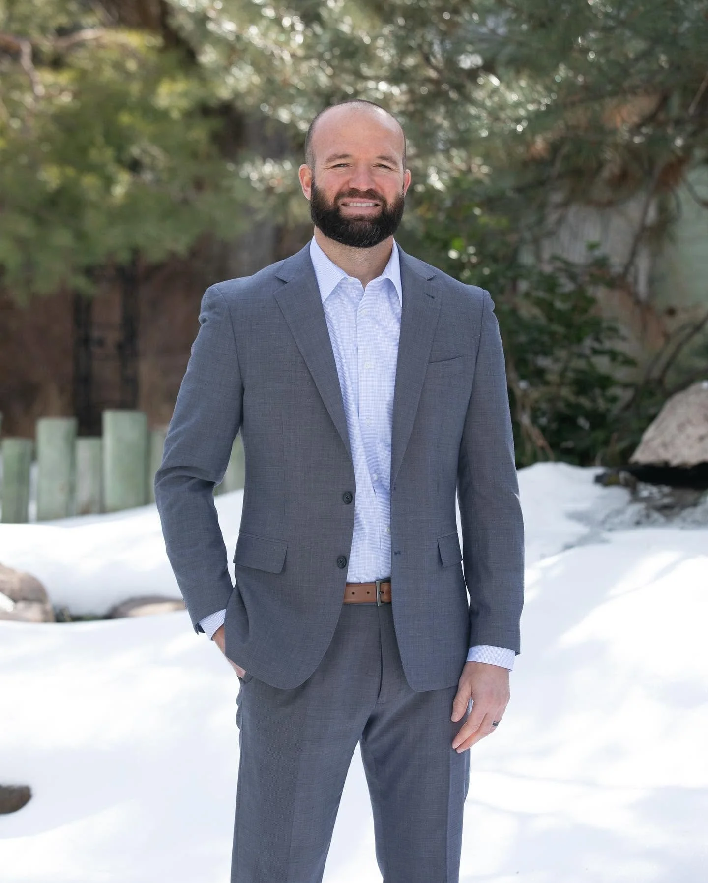 Bearded man in a gray suit standing in a snowy forest