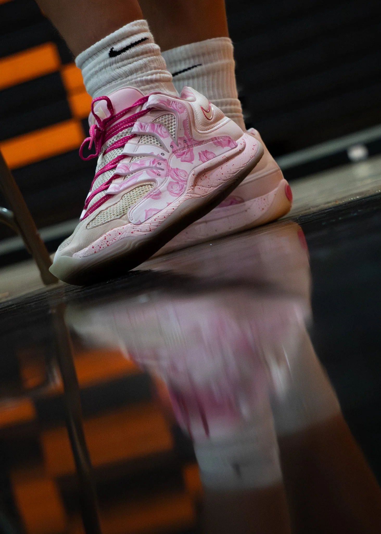 Close-up of pink floral Nike sneakers with white crew socks on gym equipment.