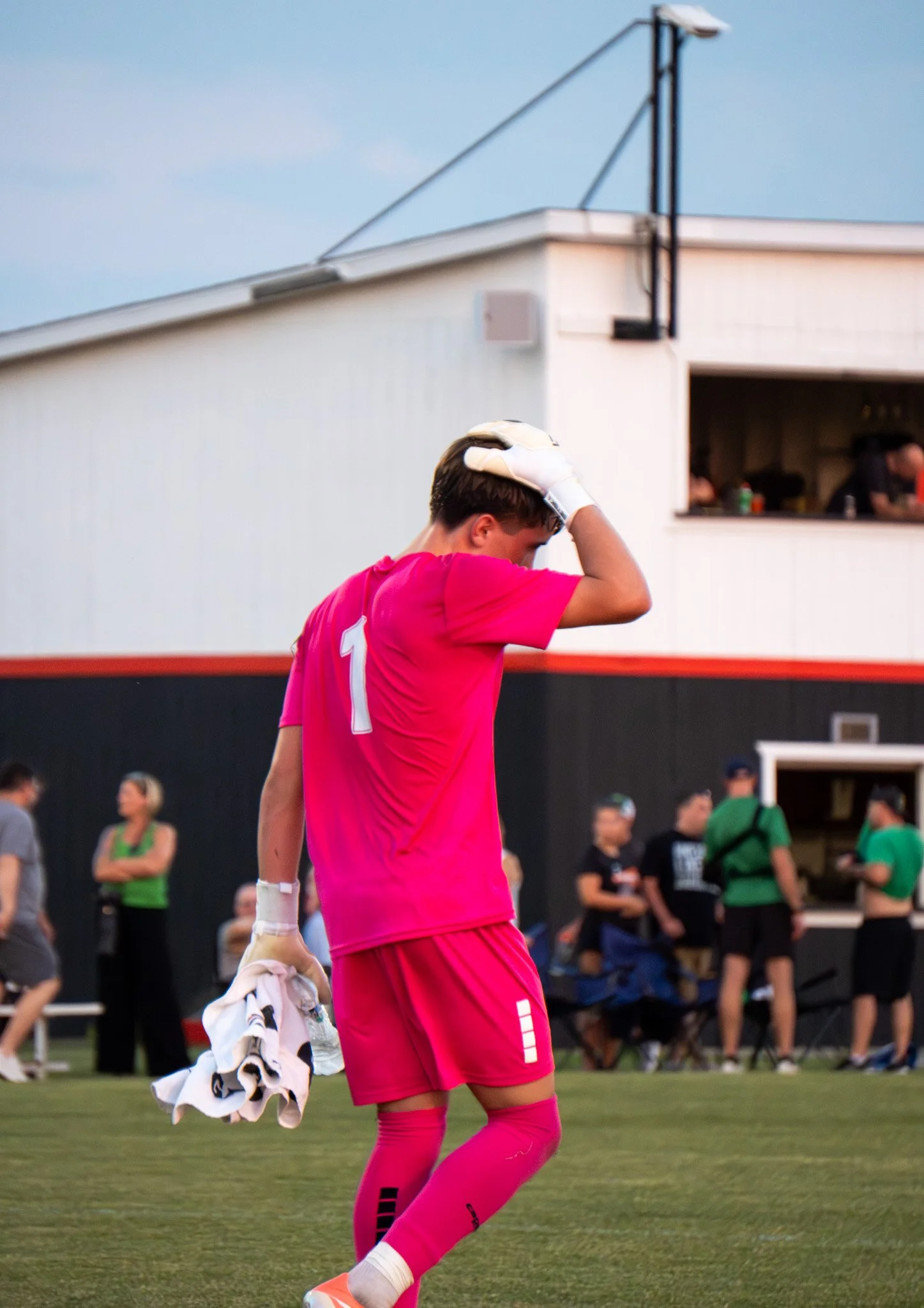 Soccer player in a pink uniform adjusting goalkeeper gloves while holding a towel on the field.