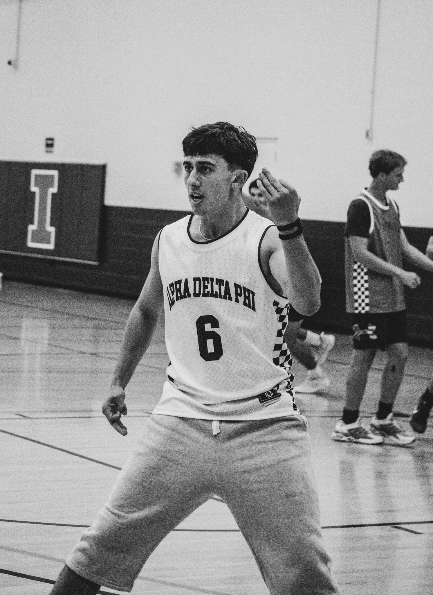 Basketball player wearing an Alpha Delta Phi jersey with number 6 gestures on an indoor court.