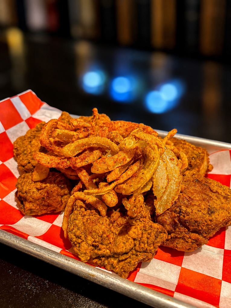 Tray of crispy fried chicken topped with fried onion rings on red-and-white checkered paper