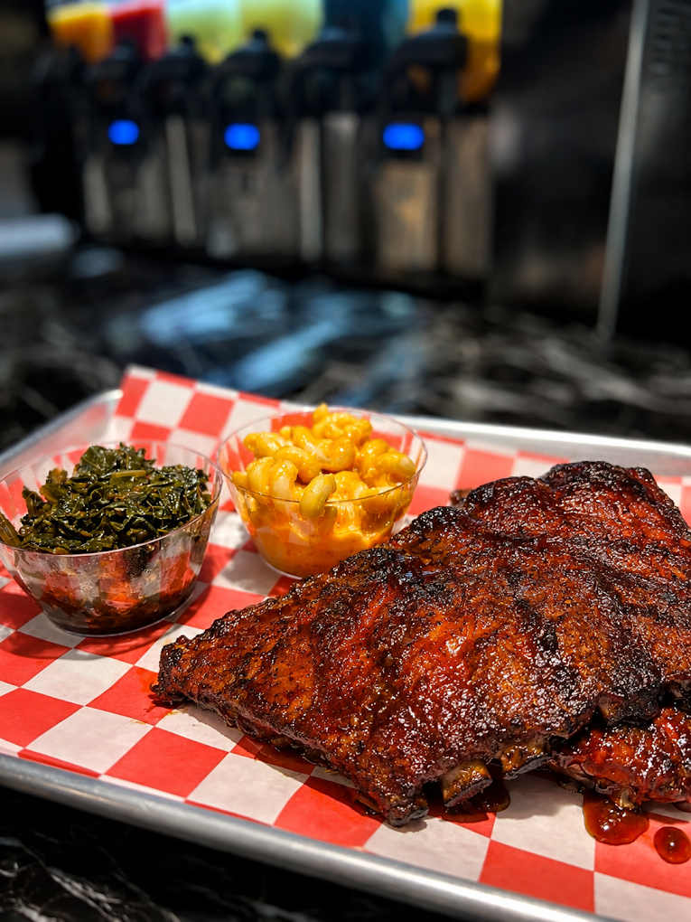 Barbecue ribs served with macaroni and cheese and collard greens on a red-and-white checkered tray