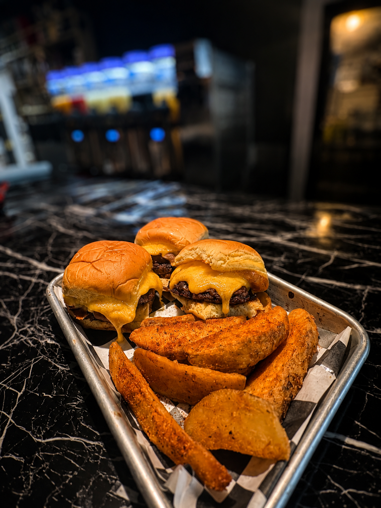 Tray of three cheeseburgers and seasoned potato wedges on a black marble table