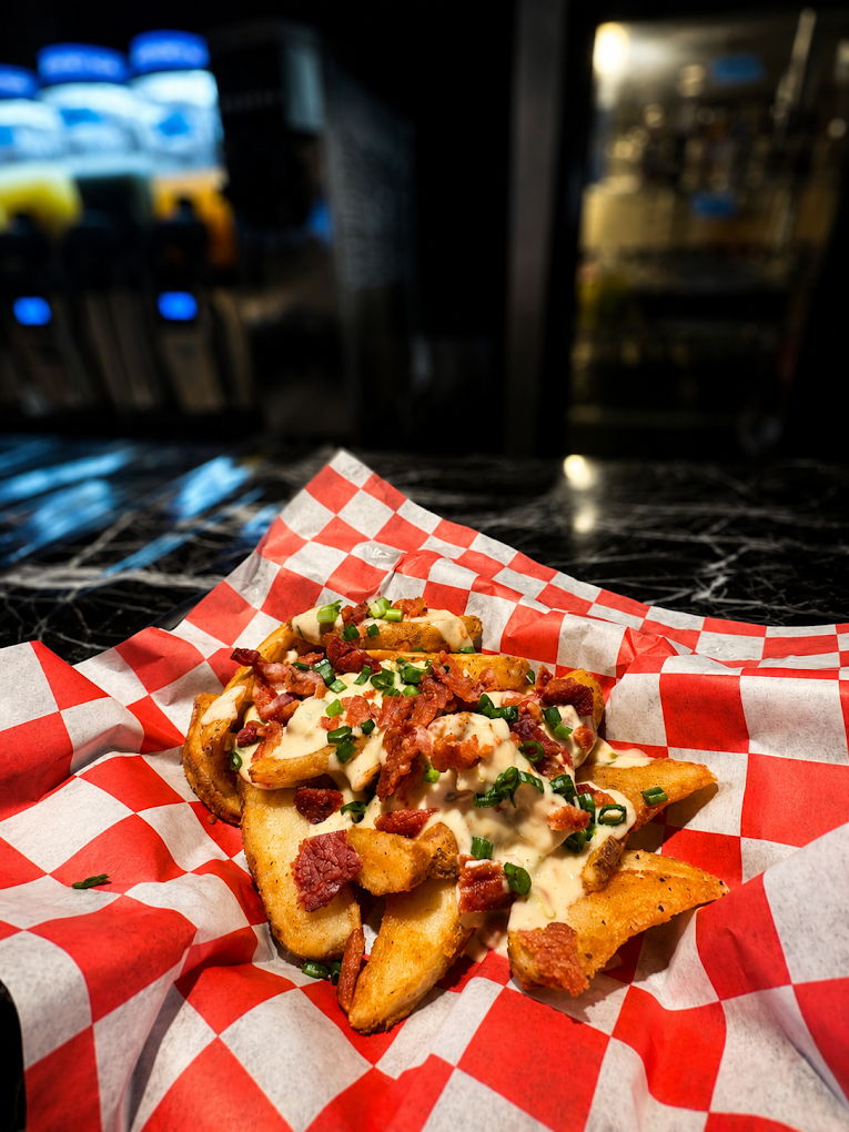 Loaded fries topped with cheese sauce, bacon, and green onions on red-and-white checkered food paper
