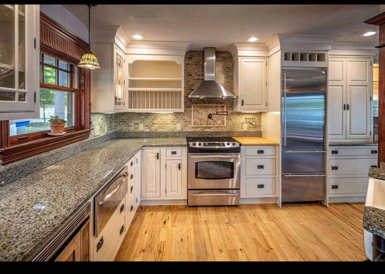 Traditional kitchen with granite countertops, white cabinets, stainless steel appliances, brick backsplash, and hardwood flooring