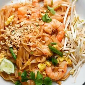 Pad Thai with shrimp, bean sprouts, crushed peanuts, lime wedges, cilantro, and scrambled egg