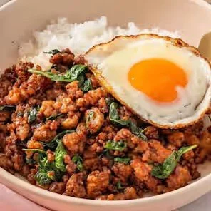 Bowl of spicy ground meat with basil, white rice, and a fried egg