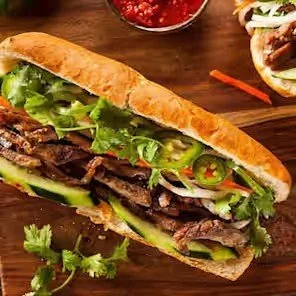 Vietnamese banh mi sandwich with grilled meat, cucumber, cilantro, lettuce, and sliced jalapeños on a wooden table