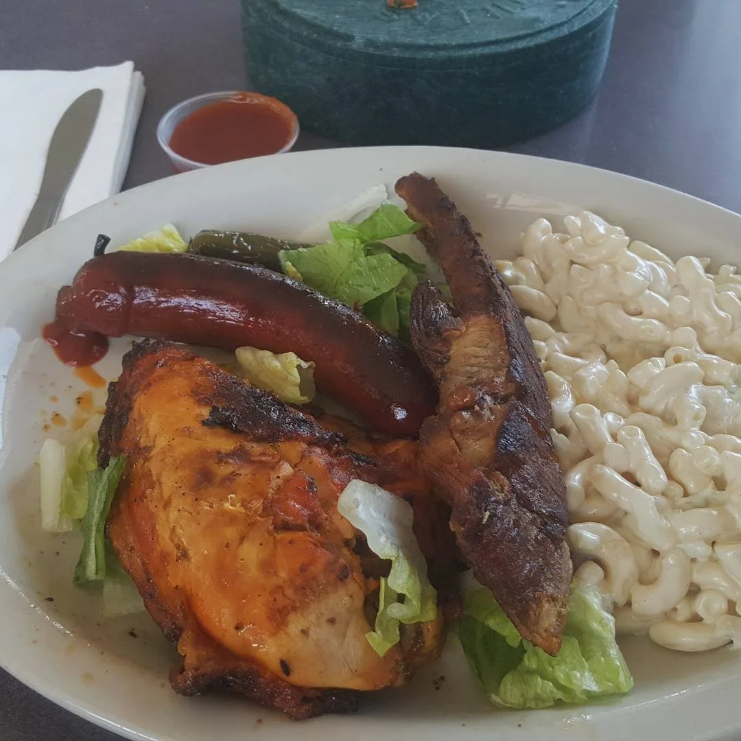 Plate of barbecue chicken, sausage, ribs, macaroni salad, lettuce, pickles, and dipping sauce