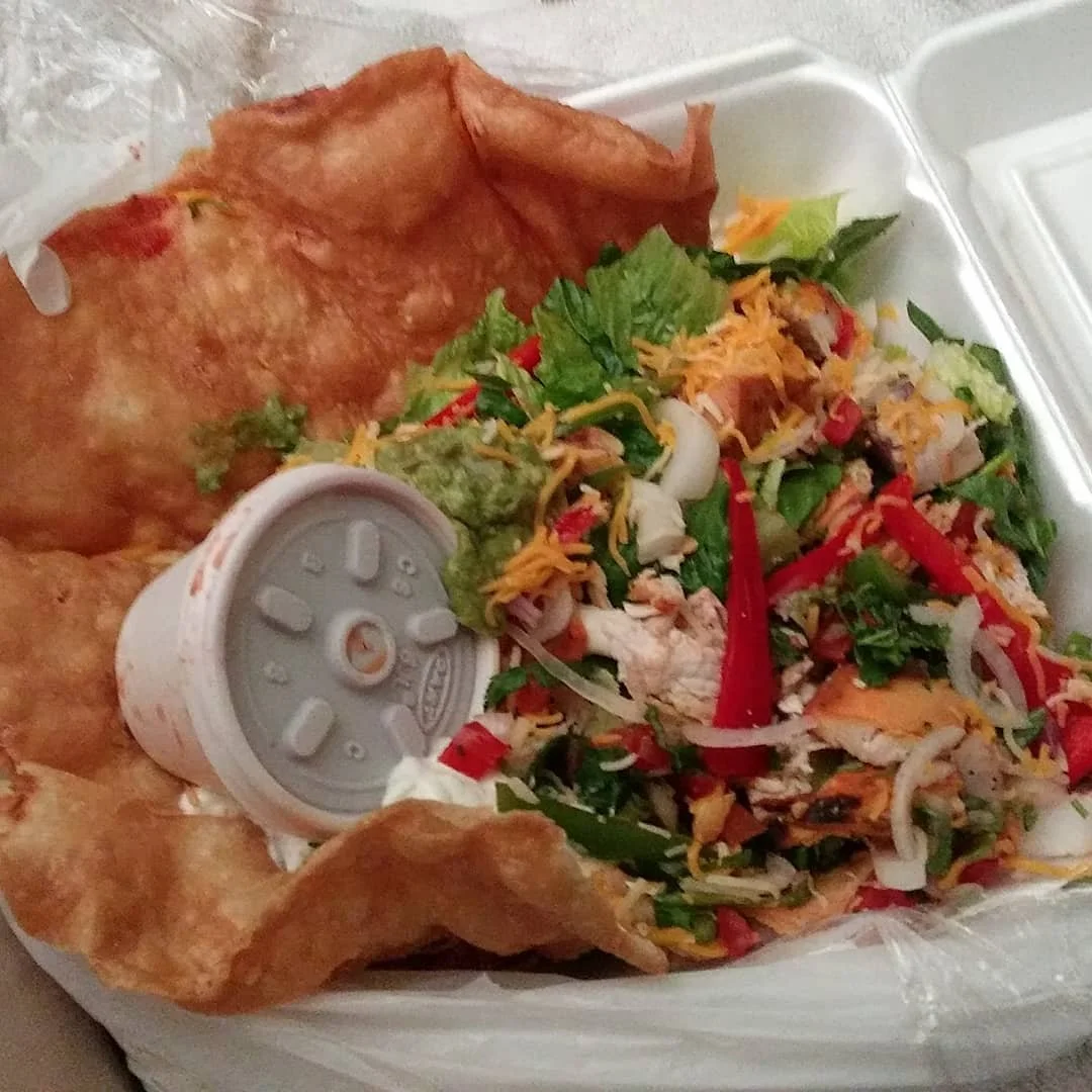 Takeout container with crispy fried wonton chips, chopped chicken salad, vegetables, shredded cheese, and dipping sauce