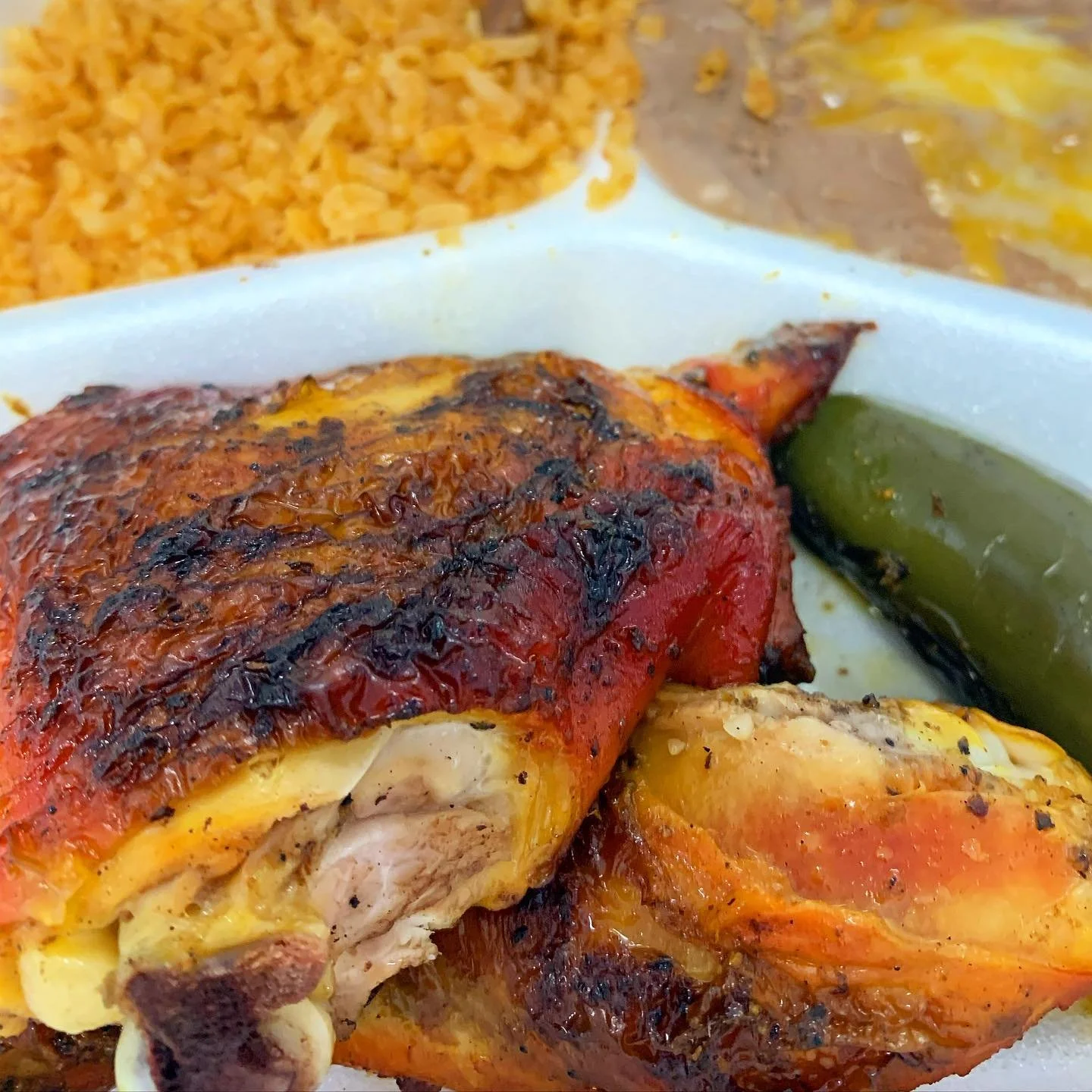Close-up of grilled chicken with charred skin, roasted vegetables, green pepper, and seasoned rice on a plate