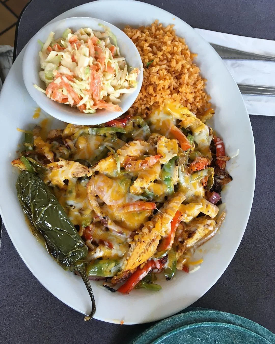 Cheesy fajita-style grilled chicken and vegetables with Mexican rice, coleslaw, and a roasted pepper on a plate