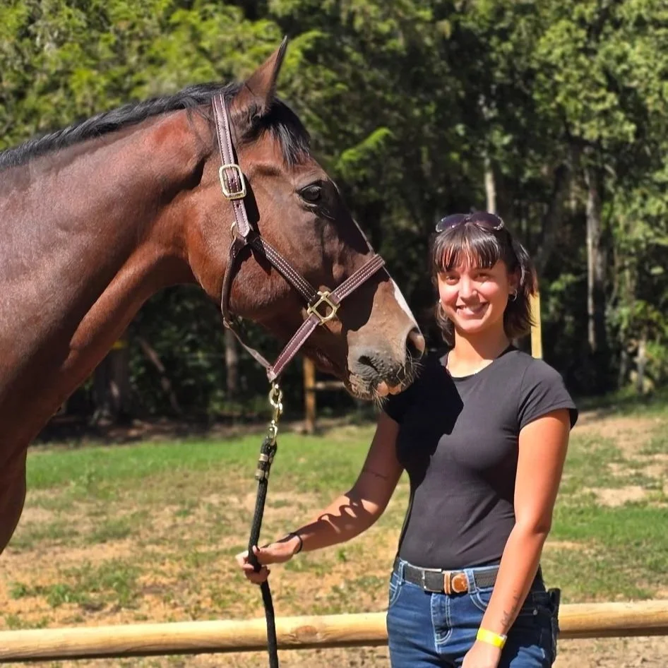 Woman holding a lead rope beside a brown horse outdoors