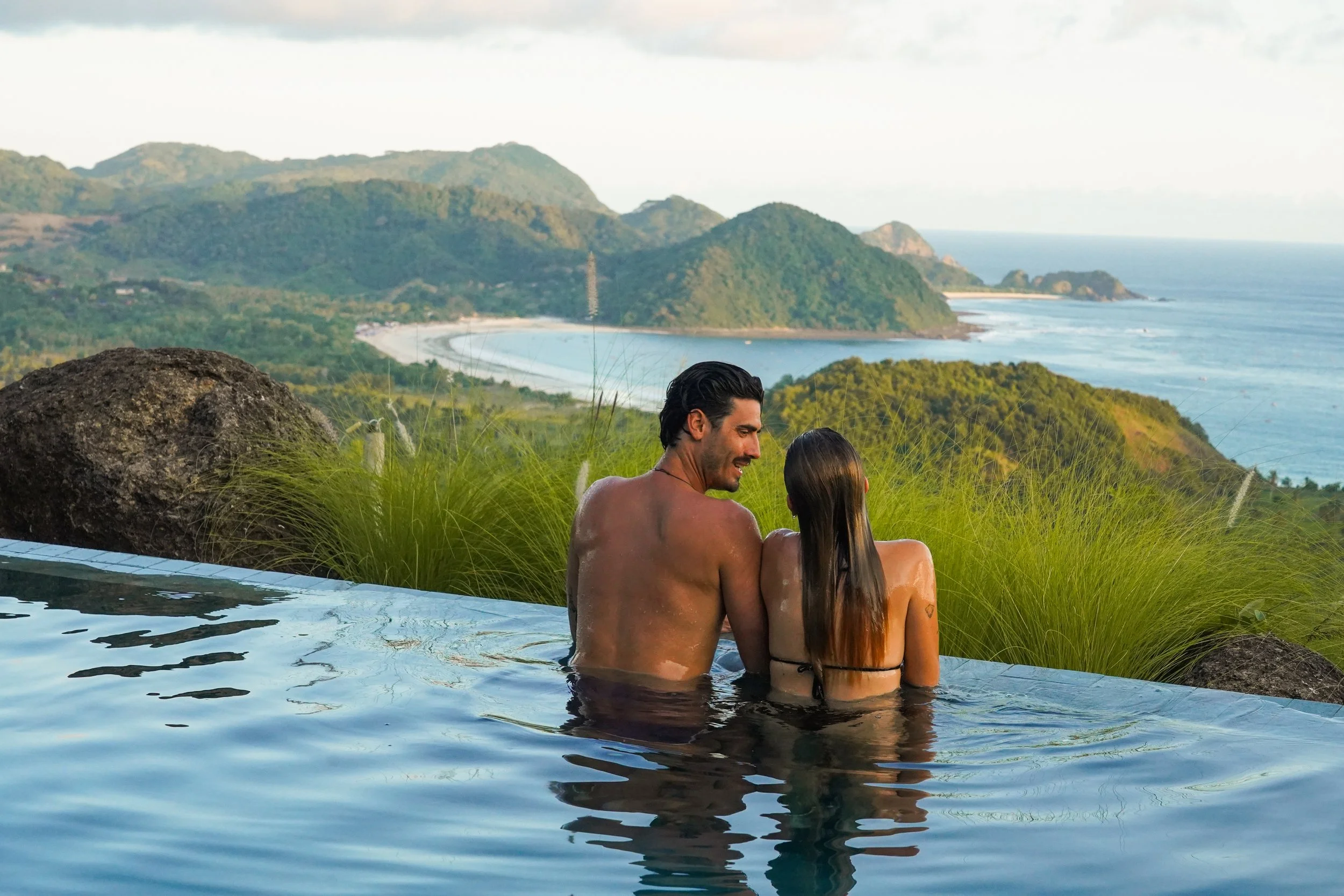 Couple relaxing in the infinity pool at Villa Kai Lani, looking out over Selong Belanak Bay, South Lombok