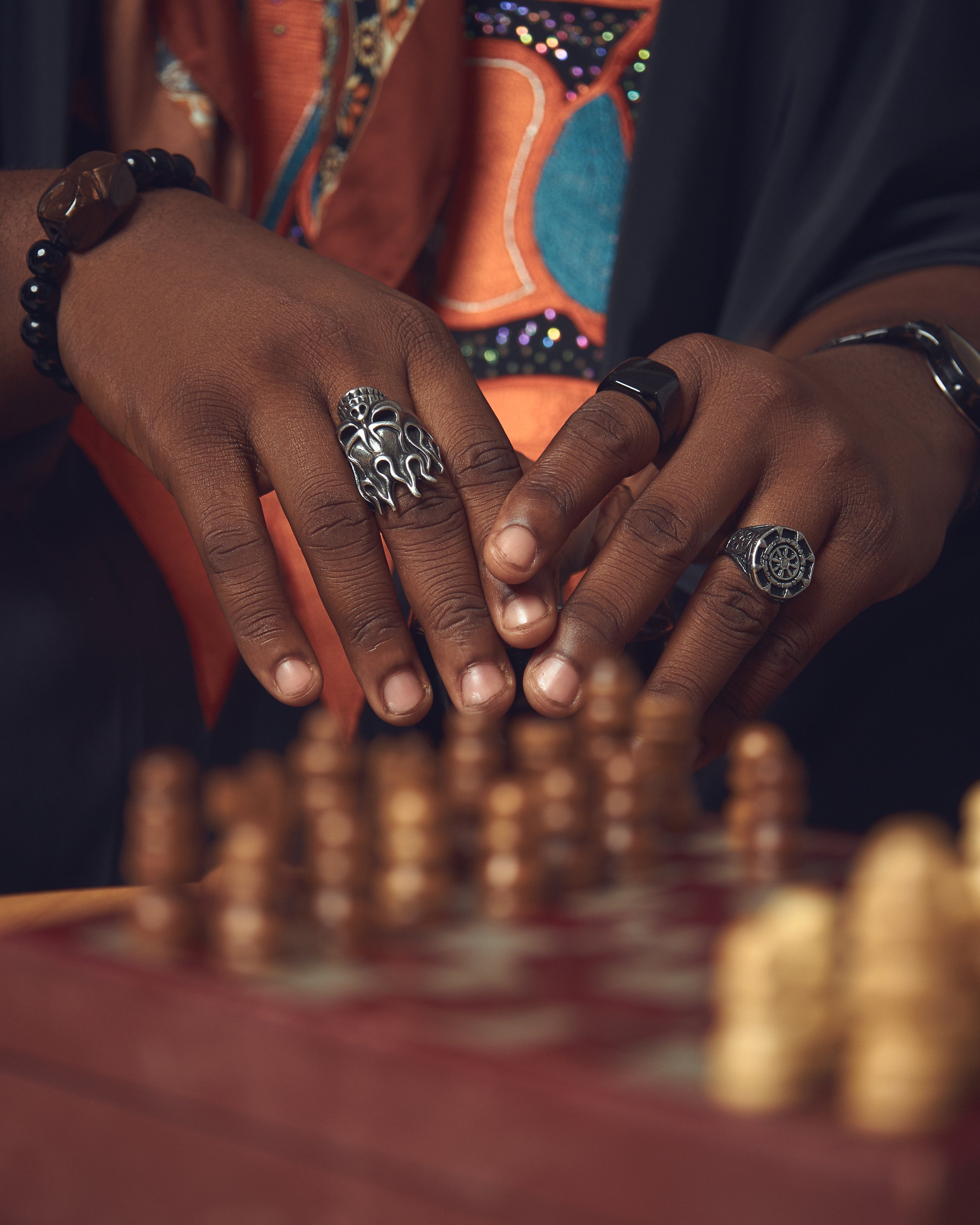 Close-up of clasped hands wearing ornate silver rings, black bracelets, and colorful patterned clothing.