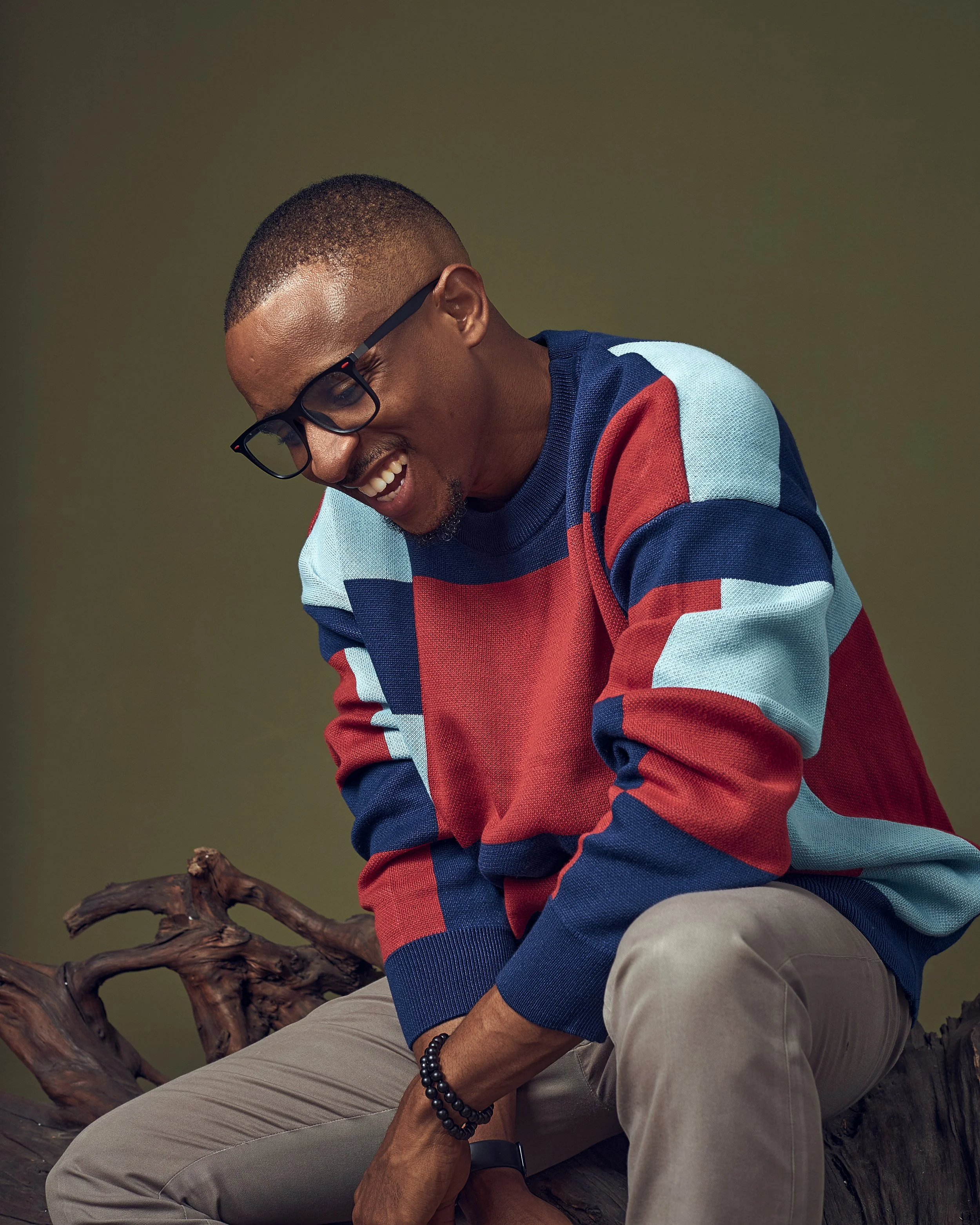 Lifestyle portrait of a smiling man wearing a colourful striped jumper and glasses, captured by London portrait photographer Ade West.