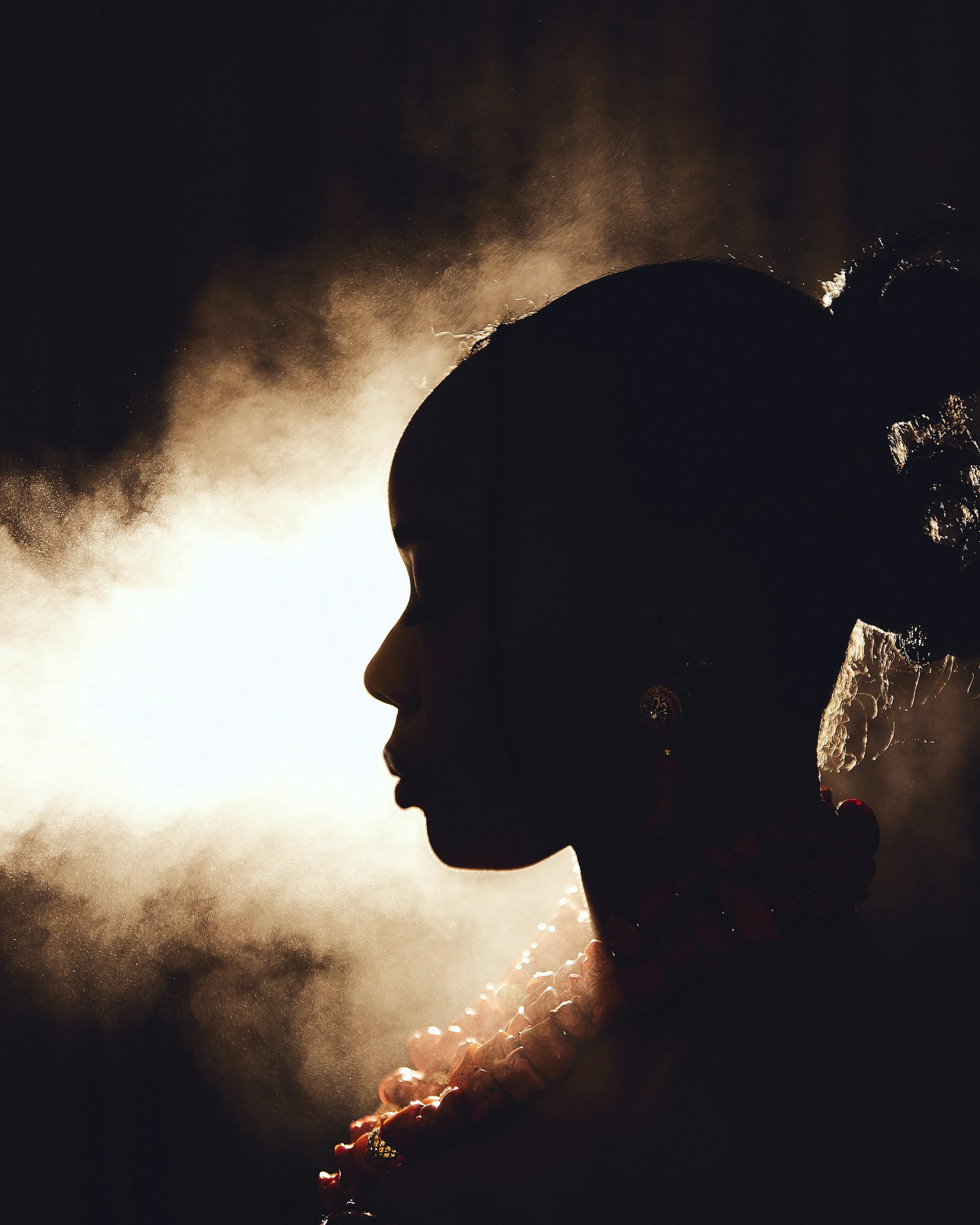 Silhouetted person in profile wearing a wide-brimmed hat, illuminated by warm sunlight and surrounded by smoke.