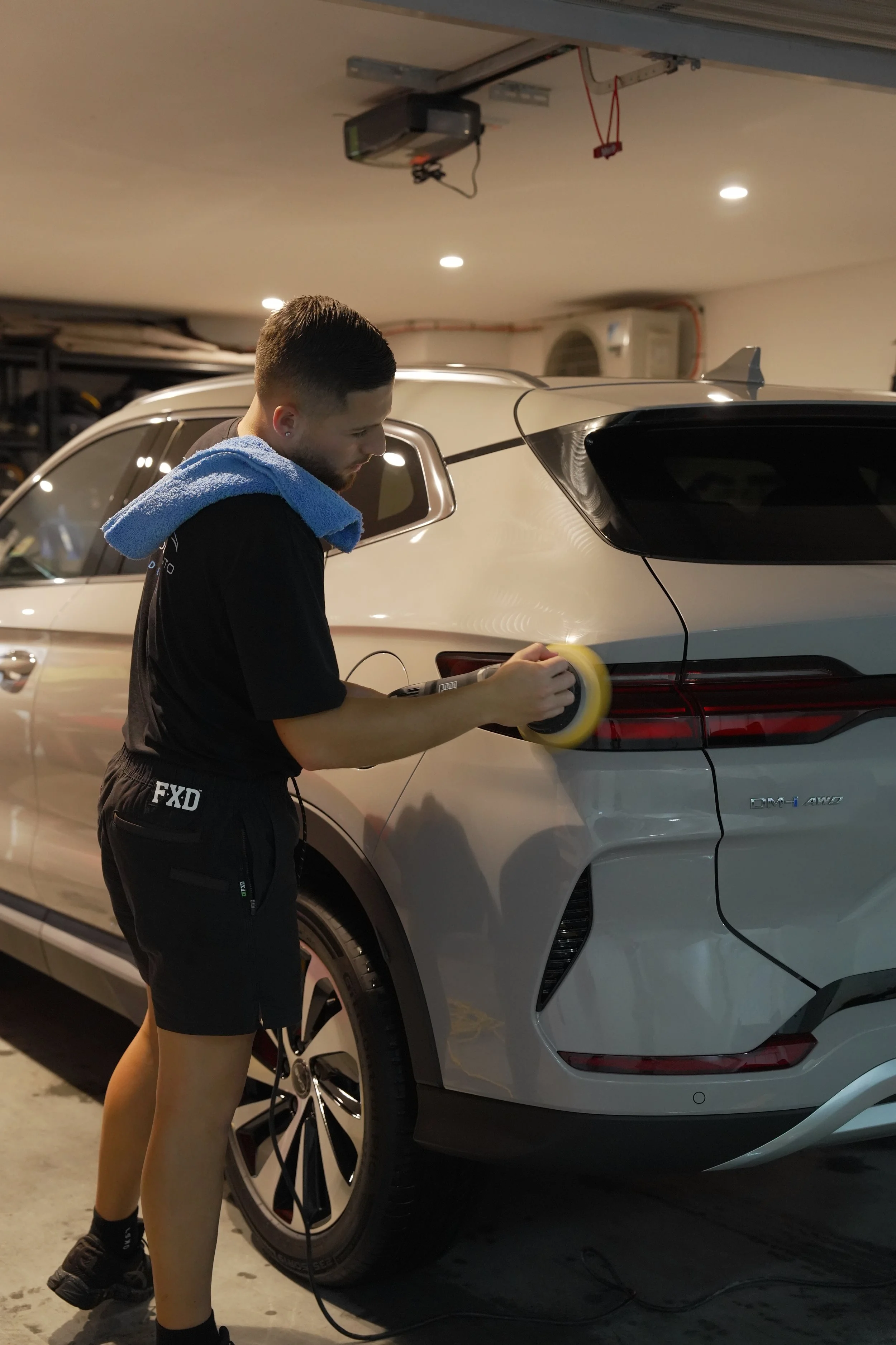 Detailer polishing the rear of a white BYD electric SUV in a garage