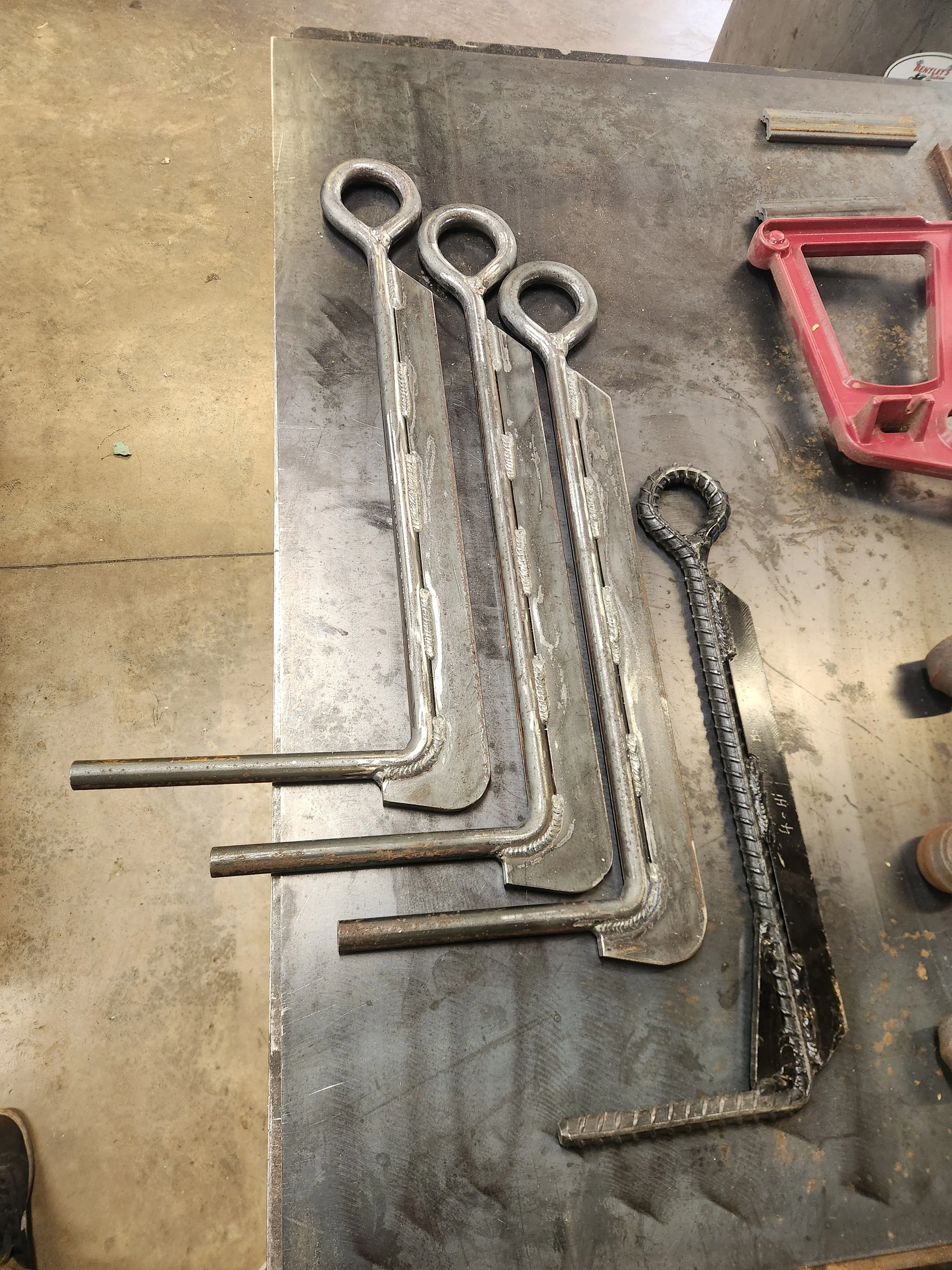Welded steel tie-down anchors and metal brackets arranged on a workshop welding table.