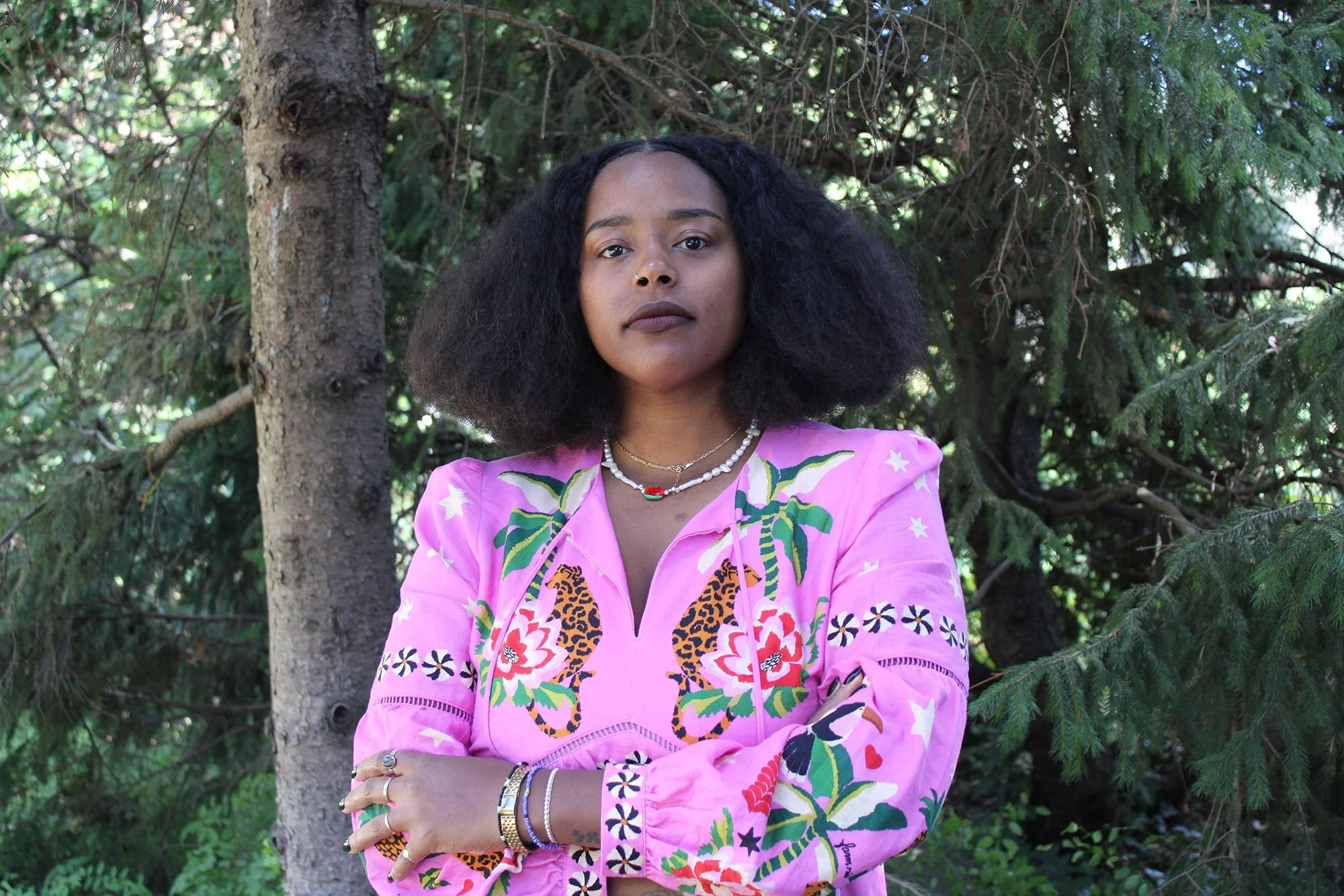Woman with natural hair wearing a colorful pink floral jacket, standing in a wooded outdoor setting