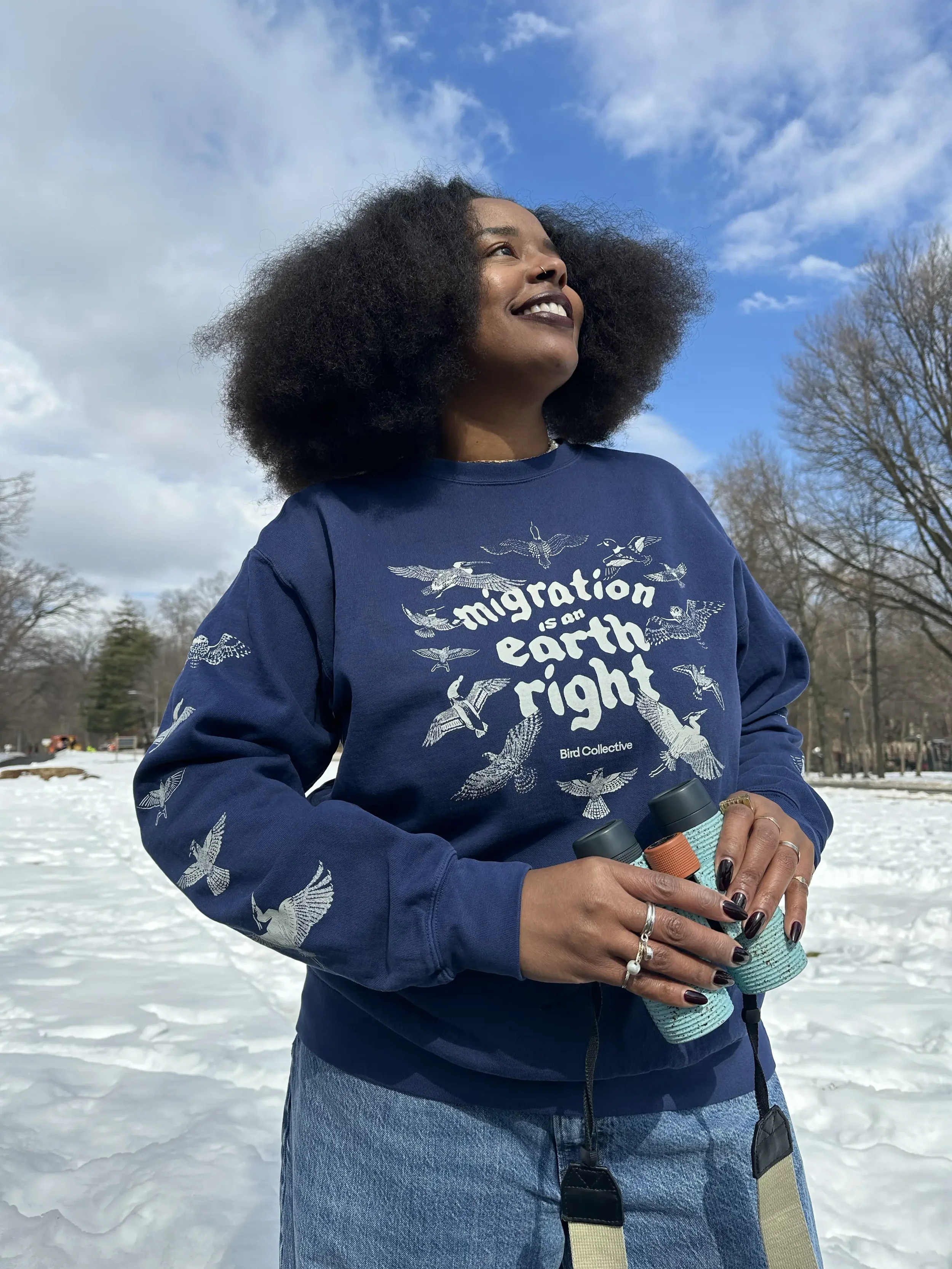 Smiling Black woman with curly hair holding binoculars outdoors in a snowy park