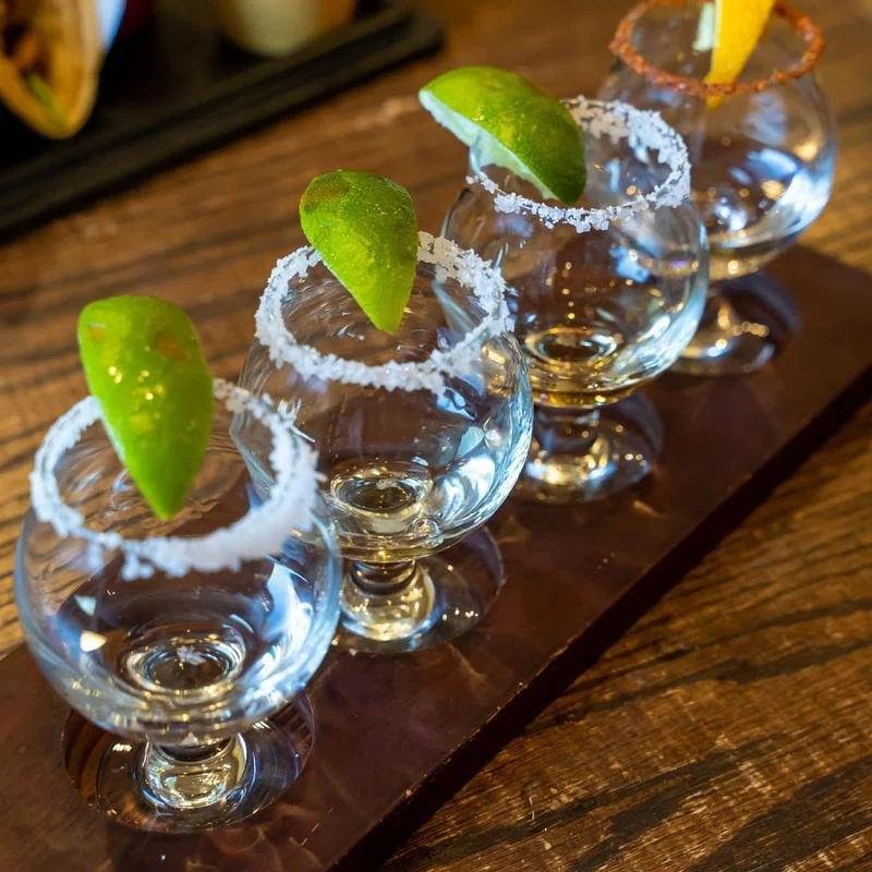 Four empty margarita glasses with salt-rimmed edges and lime wedges arranged on a wooden serving board.