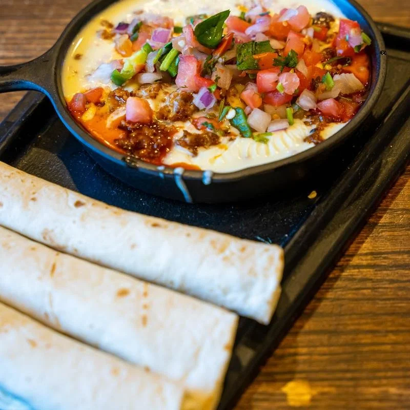 Skillet of creamy queso dip topped with pico de gallo and served with flour tortillas