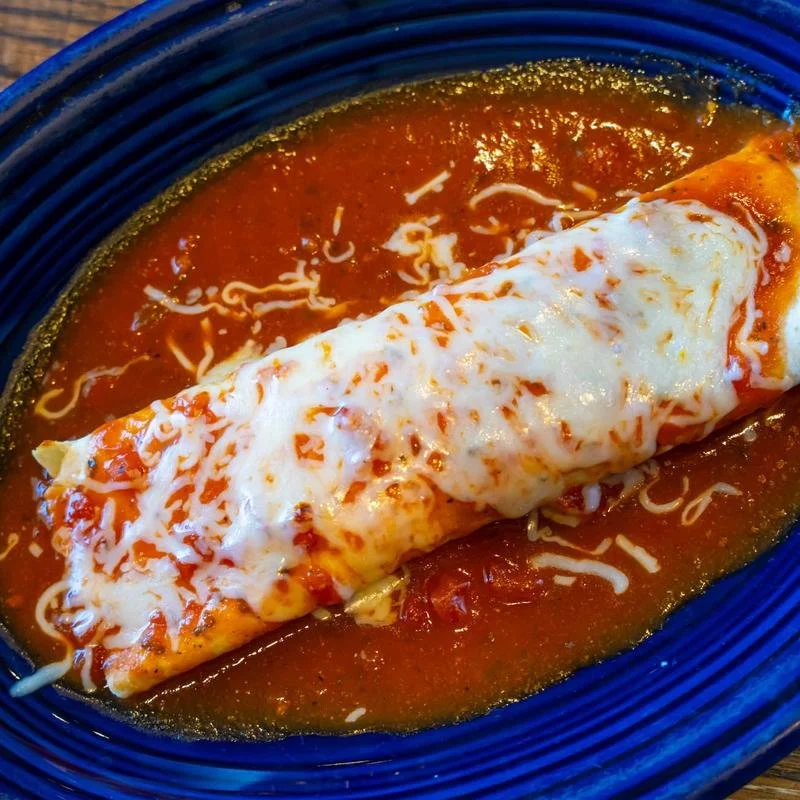 Cheese-covered enchilada served in red sauce on a blue plate
