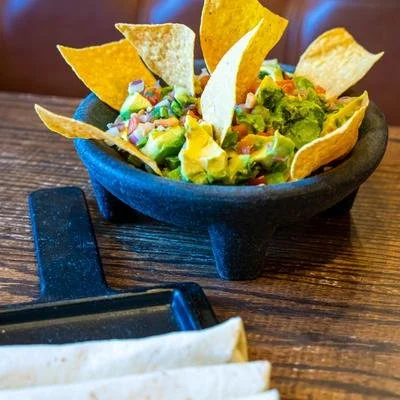 Loaded nachos with tortilla chips, guacamole, salsa, cheese, and vegetables in a black bowl