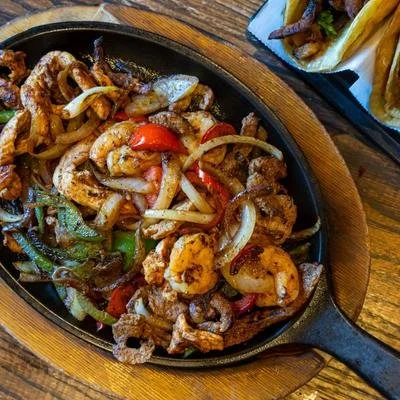 Sizzling shrimp and chicken fajitas with peppers and onions in a cast-iron skillet, served with tortillas.