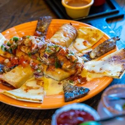 Orange plate of cheesy quesadillas topped with grilled meat, salsa, and cilantro, served with dipping sauces