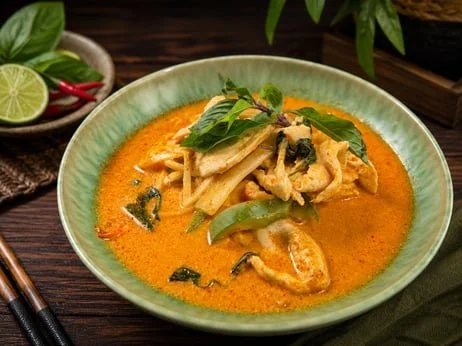 Bowl of Thai red curry with chicken, bamboo shoots, bell peppers, basil, and lime garnish