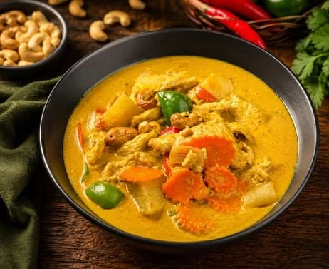 Bowl of creamy yellow chicken curry with vegetables, cashews, and chili peppers