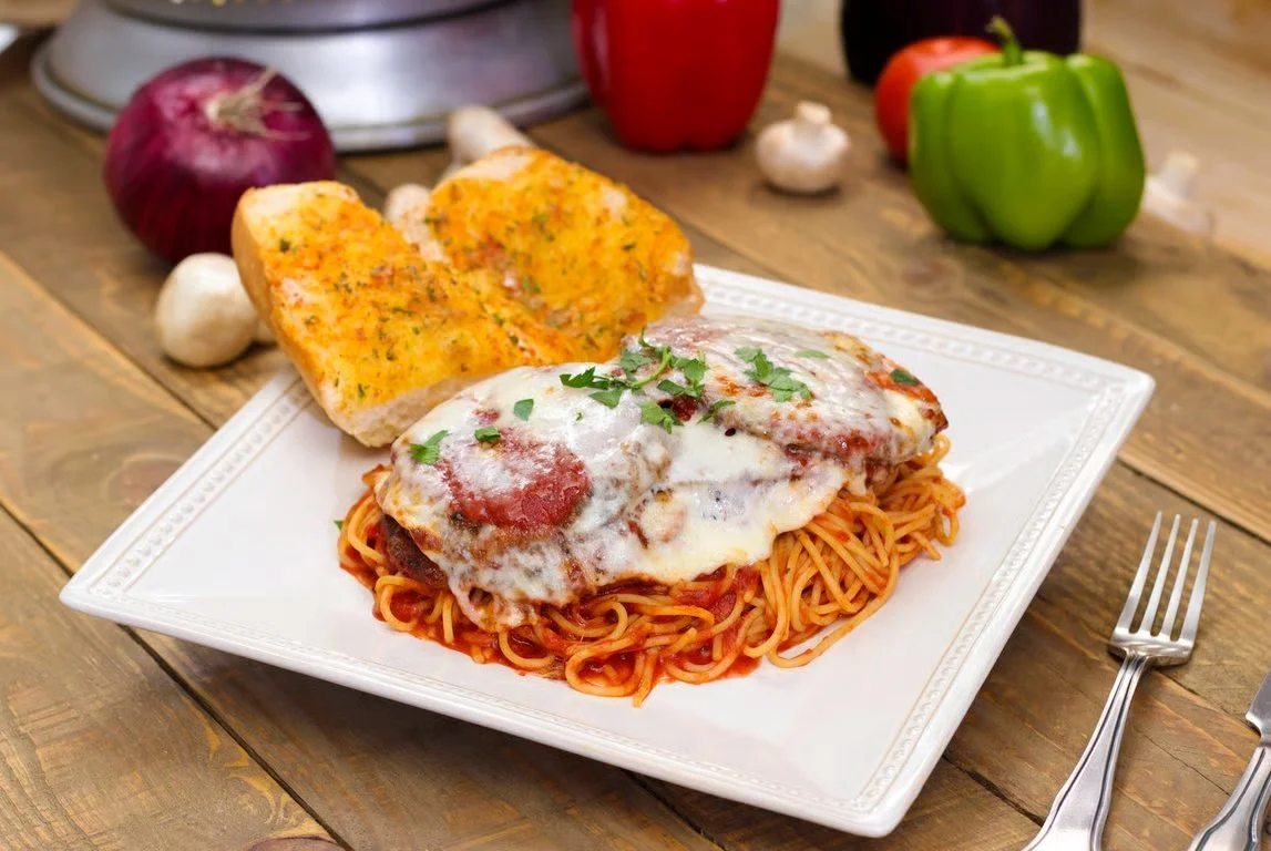 Chicken Parmesan with melted mozzarella over spaghetti marinara, served with garlic bread on a white plate