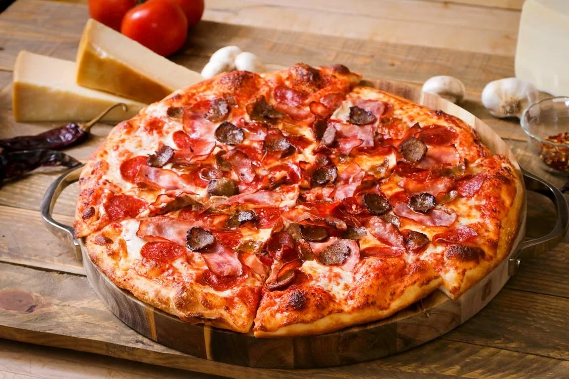 Loaded meat-lover's pizza with pepperoni, ham, sausage, and mushrooms on a wooden serving board