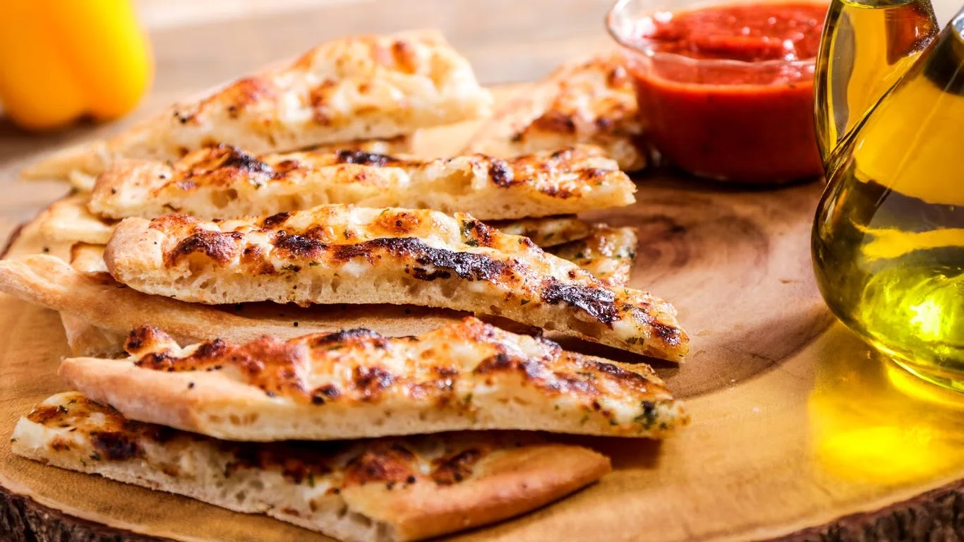 Stack of grilled flatbreads with tomato dipping sauce and olive oil on a wooden board