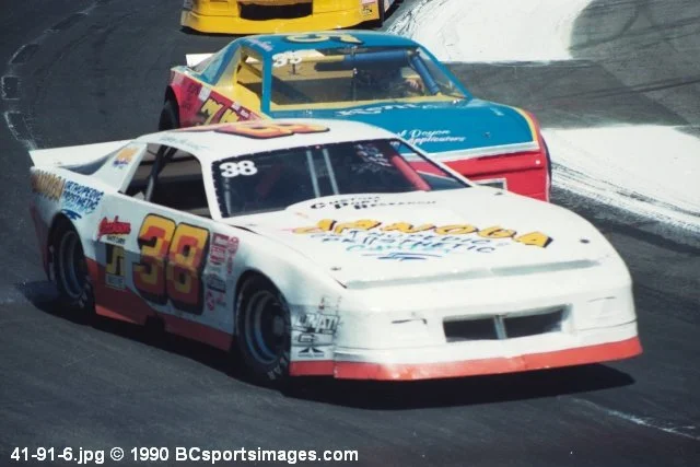 Vintage stock car race with white No. 88 car leading teal and red race cars on a banked track