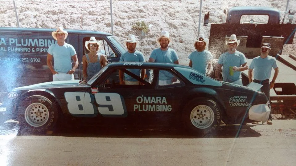 Vintage racing car No. 89 sponsored by O'Mara Plumbing, with a team of six people standing beside it.
