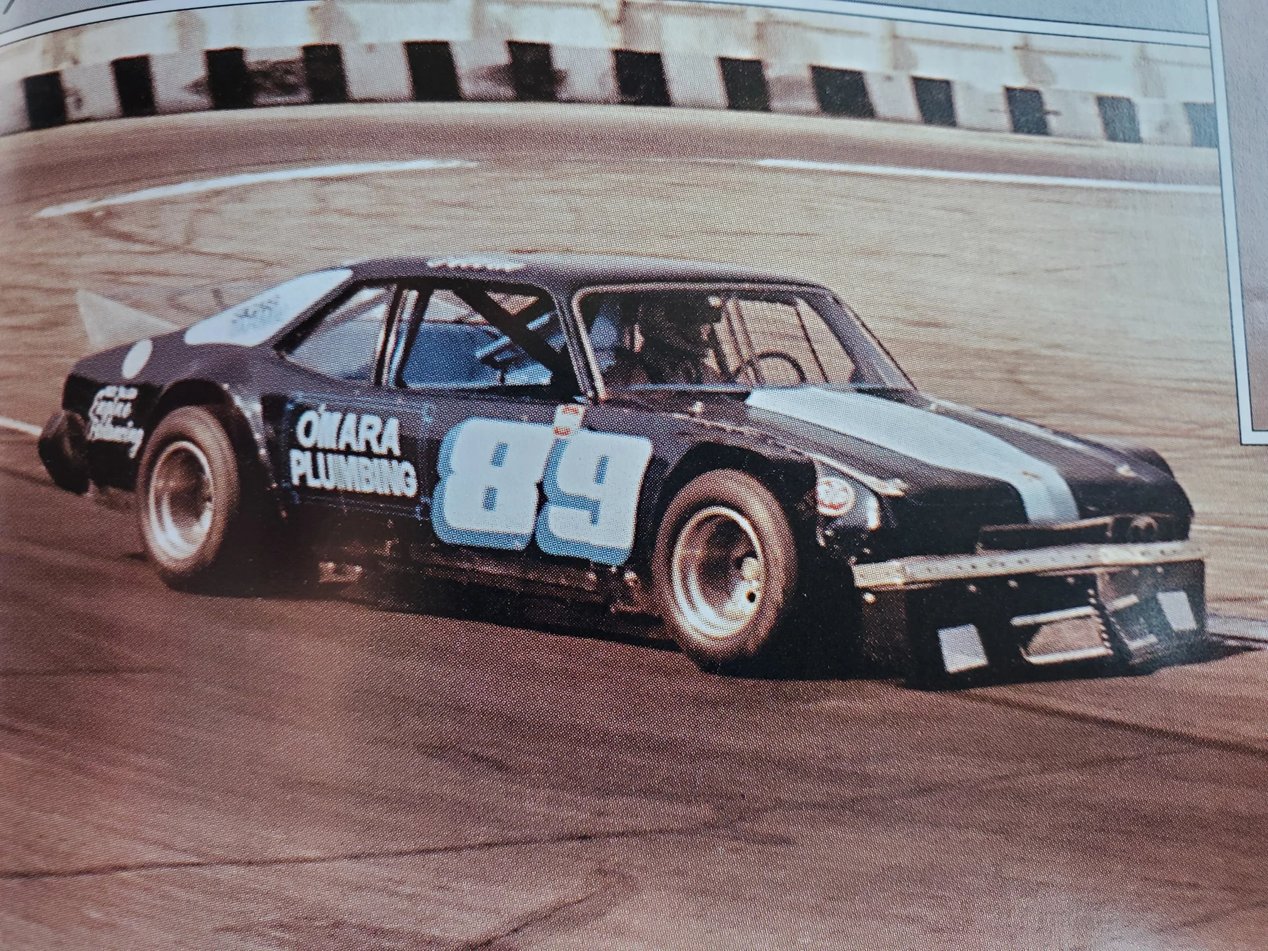 Vintage blue-and-white race car with number 38 driving on a paved racetrack