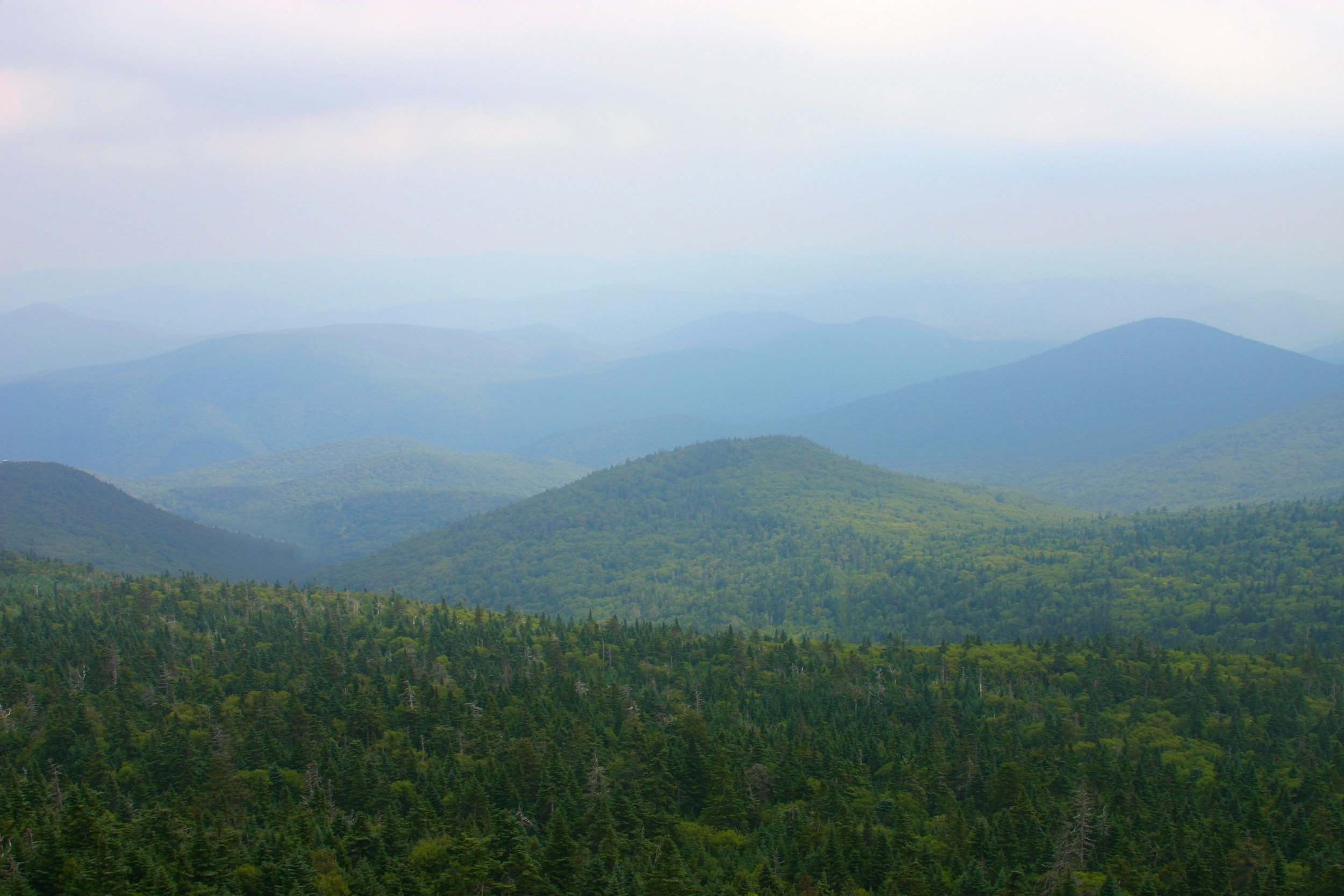 Forested Vermont mountains fading into the distance beneath a hazy sky