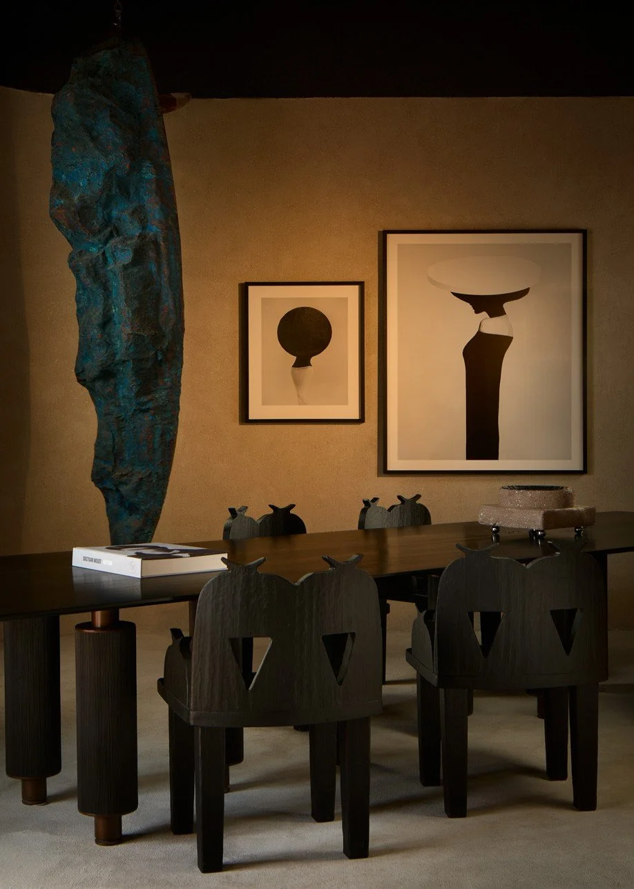 Mesa y sillas oscuras junto a una escultura azul y obras enmarcadas.