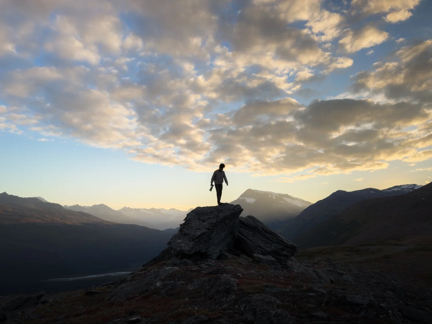 Hiker silhouetted on a mountain ridge beneath a dramatic sky