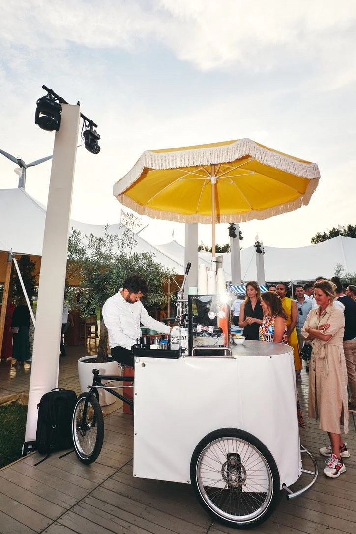A coffee bike under a yellow fringed parasol at golden hour