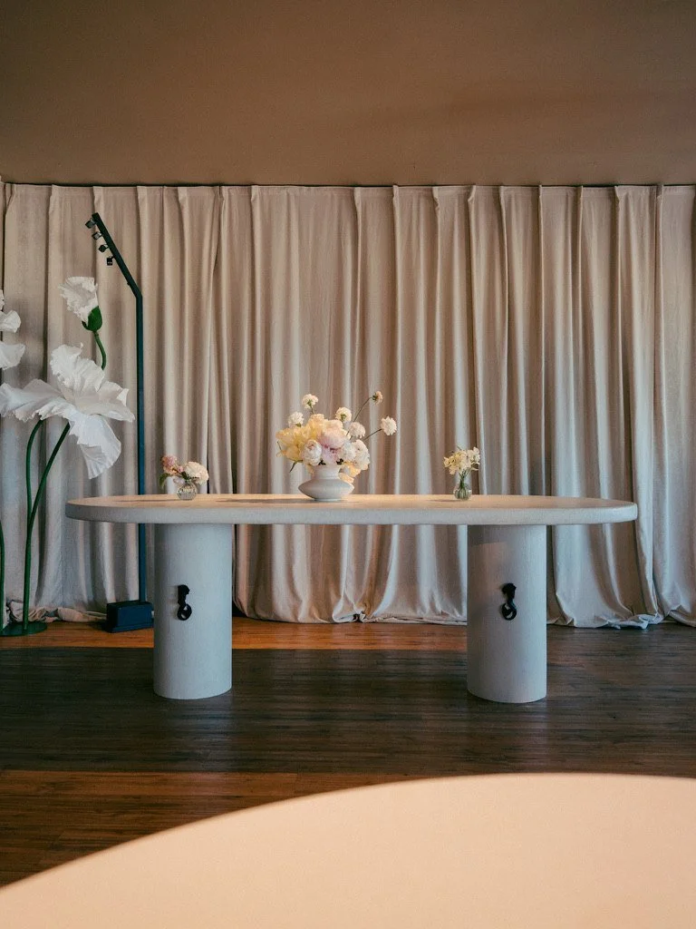A white stone table with peonies in front of linen drapes and Bloomhaus paper flowers