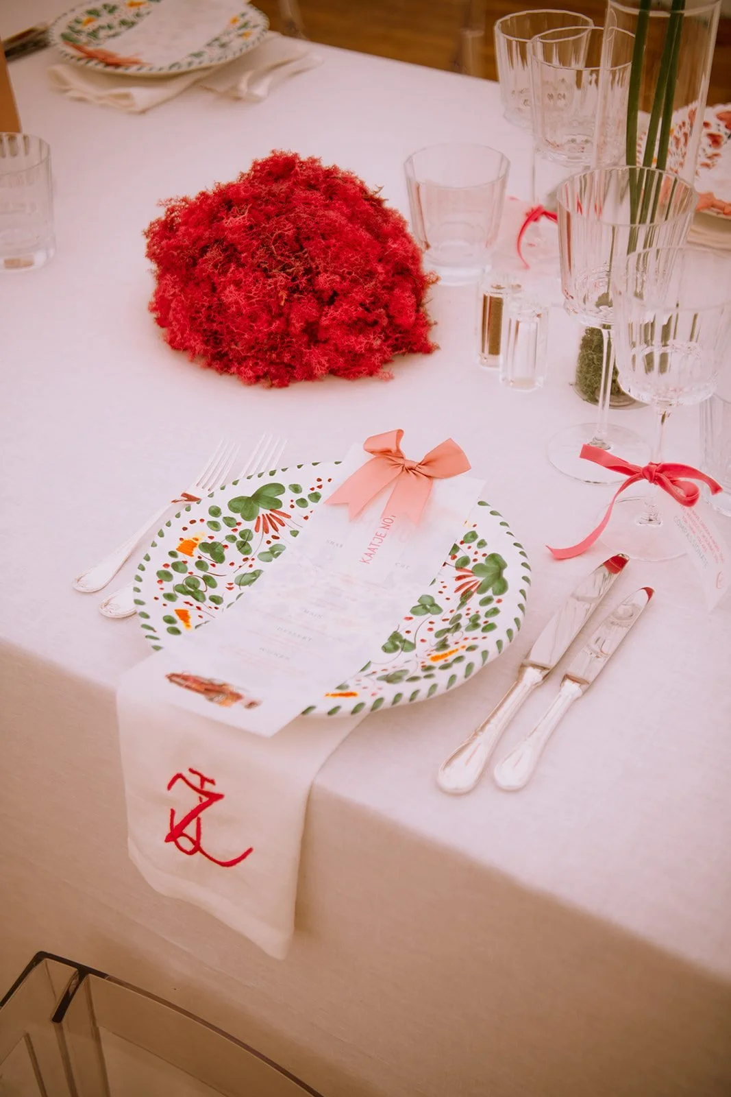 A table setting with a red flower ball, patterned plates and a pink ribbon